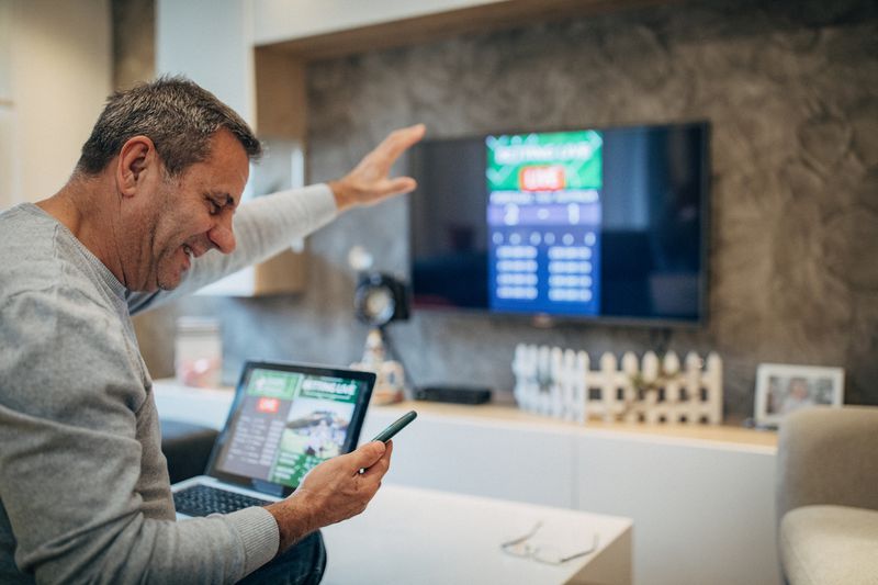 Mature man using mobile app for live betting and online gambling and watching a sports match