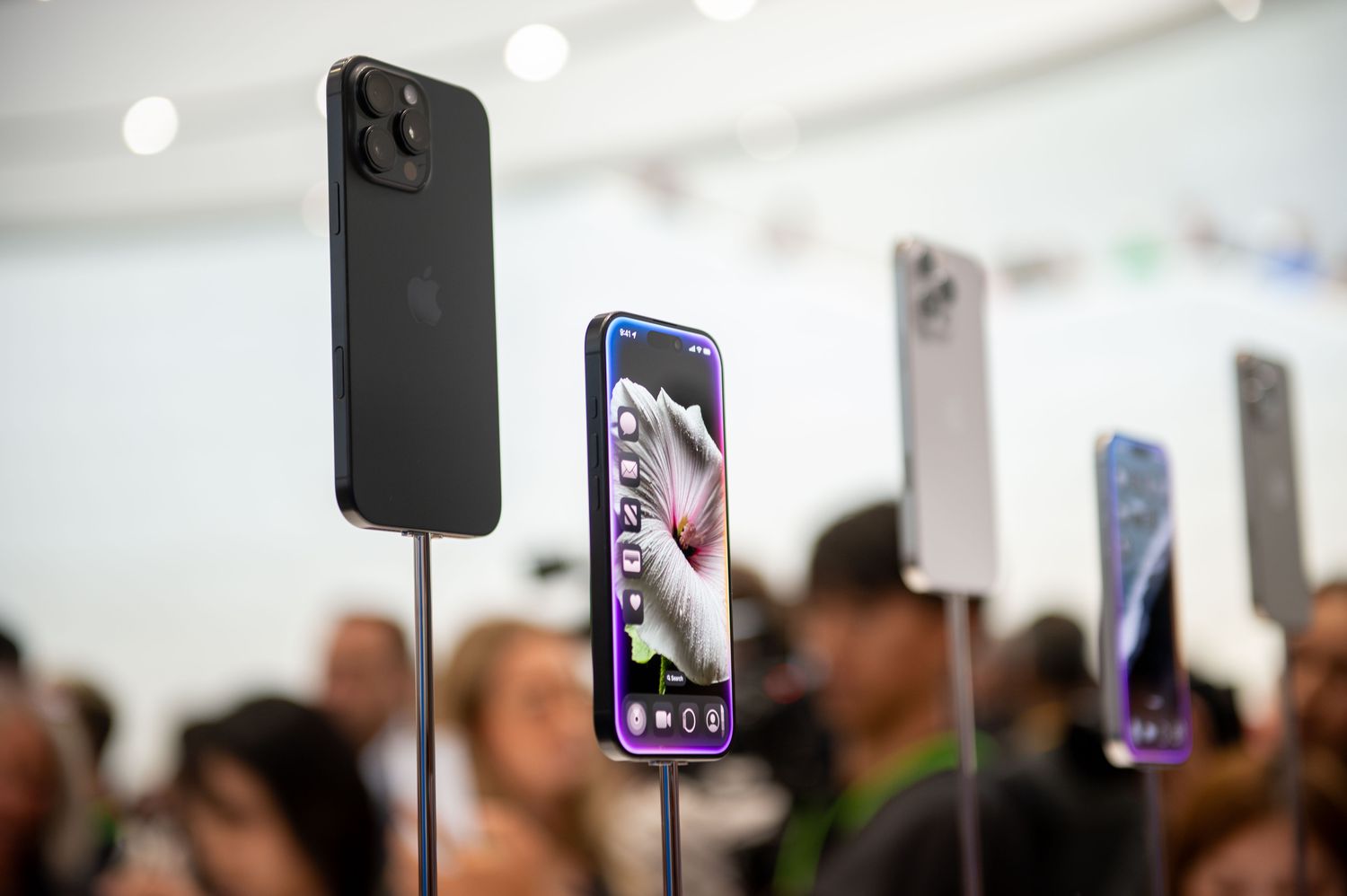 Five iPhone 16s are on display in front of a crowd of people.