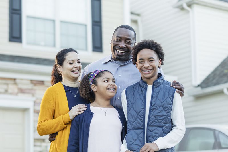An interracial Hispanic and African-American family with two children standing on the driveway in front of their house