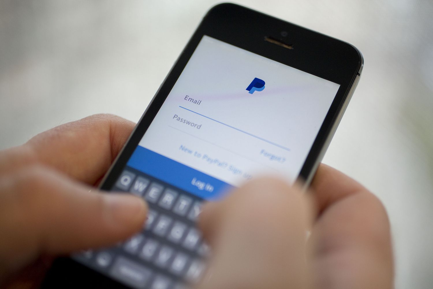 Person holding a mobile phone showing a PayPal account login page.