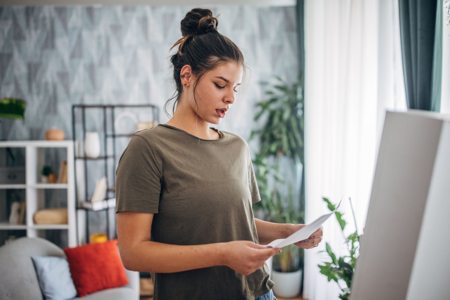 A woman stands in a living room looking concerned as she reads a letter