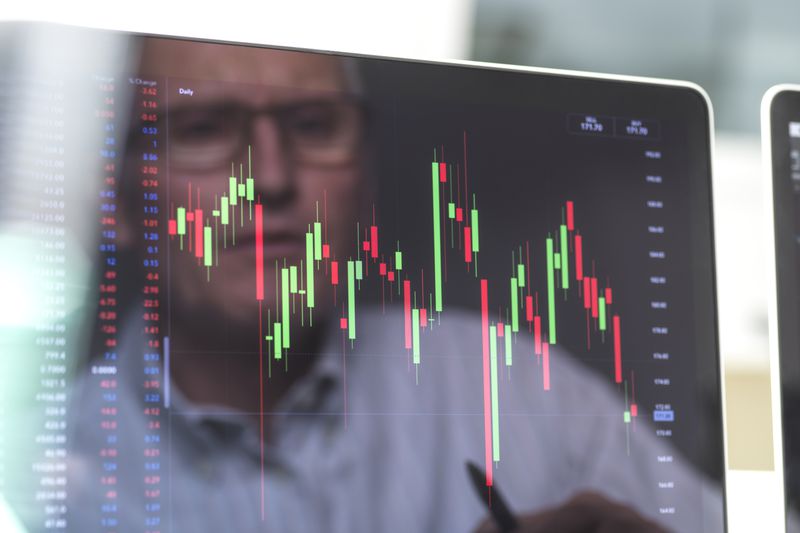 The reflection of an derivative investor appears on a computer monitor showing the price movement of the underlying stocks they are following.