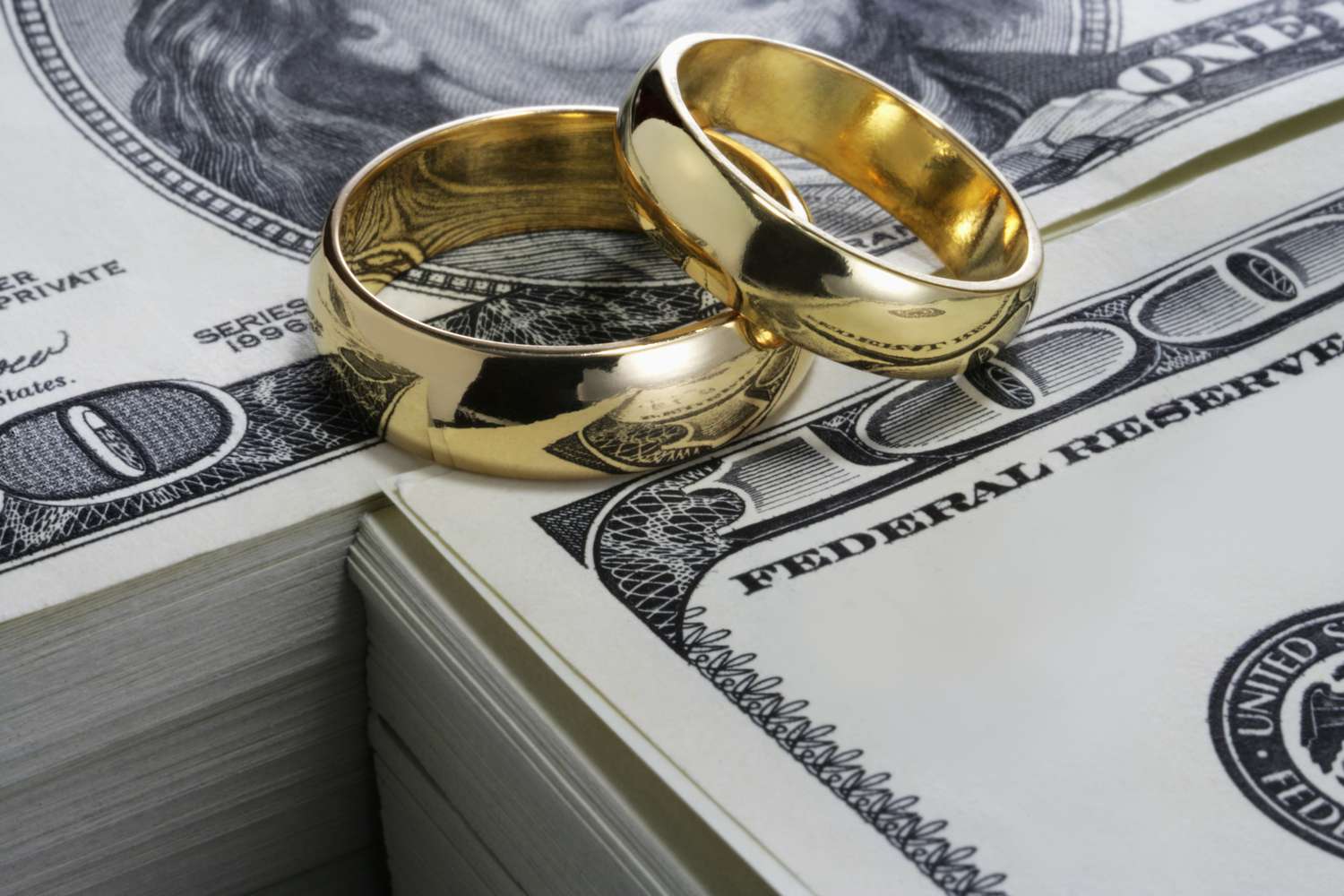 Wedding rings sit on a stack of cash.