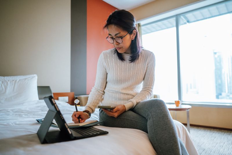 Woman researching what a deferment period is on a hotel bed