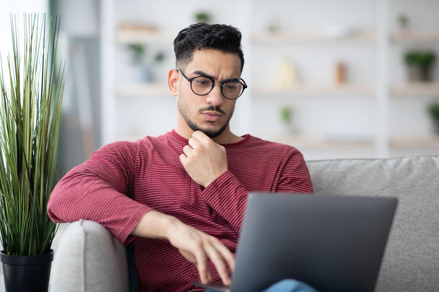 Young man on his living room sofa looking seriously at something on his laptop