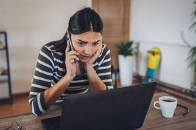 A young person staring anxiously at a laptop, phone in hand.