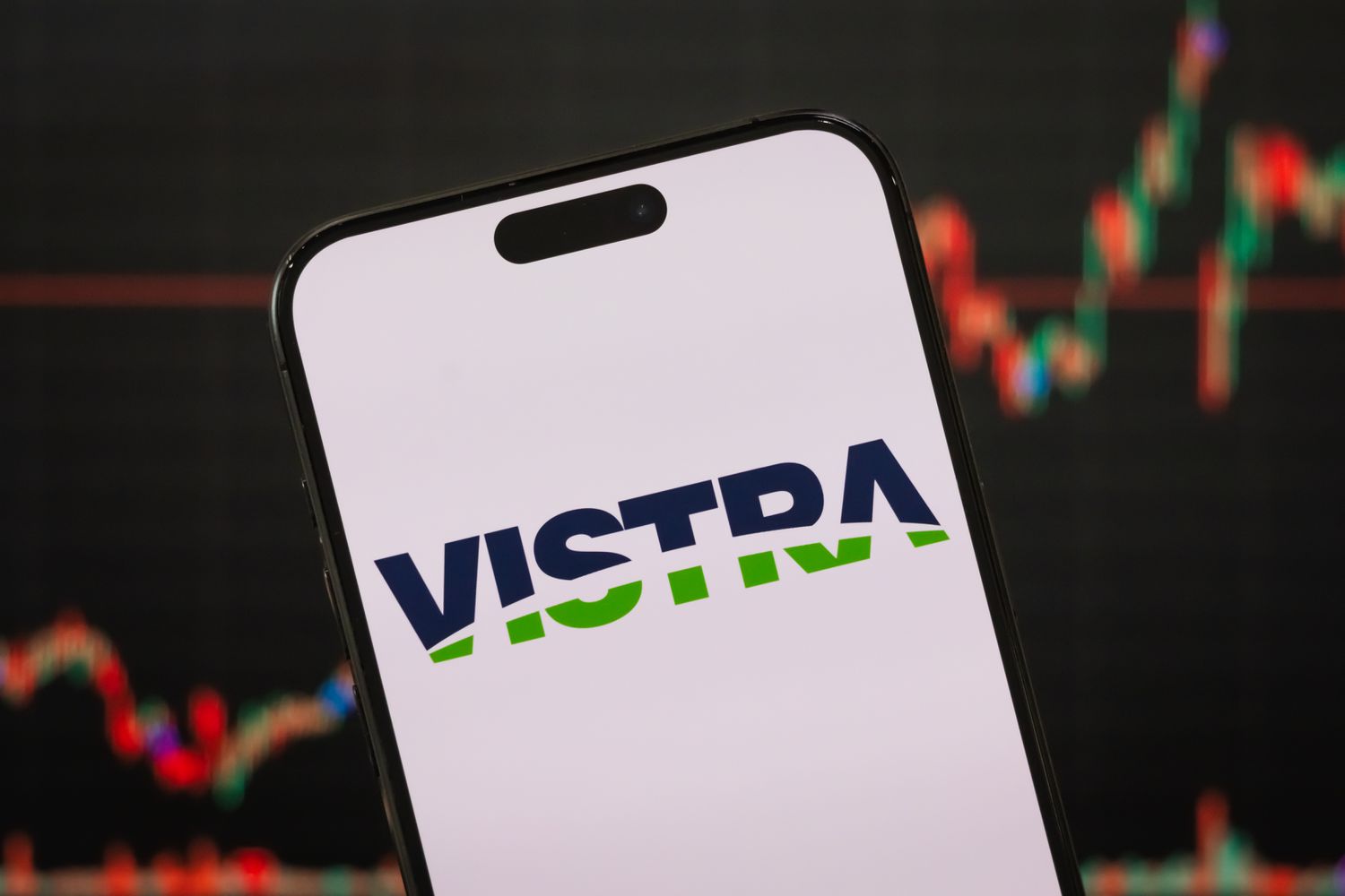 The blue and green Vistra logo is seen on a phone screen with a red and green stock chart in the background.