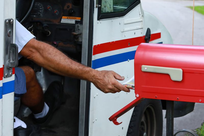 Mailman reaches out of his truck to deliver mail.