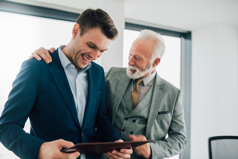 Older business man hugging younger coworker