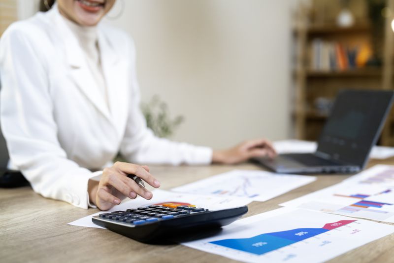 A Woman Sitting at a Desk working with a calculator and a laptop