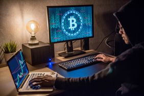 A hacker working on a desktop and laptop to hack bitcoin.