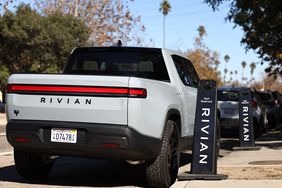 A gray Rivian truck is seen parked next to signs on a sidewalk with the Rivian logo.