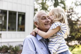 Older man holding grandchild in front of their house that is in reverse mortgage.