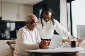 Older couple sitting in their kitchen and looking happily at mortgage rates on a laptop