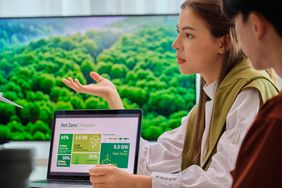 A woman speaks in a meeting with a laptop displaying emissions data.