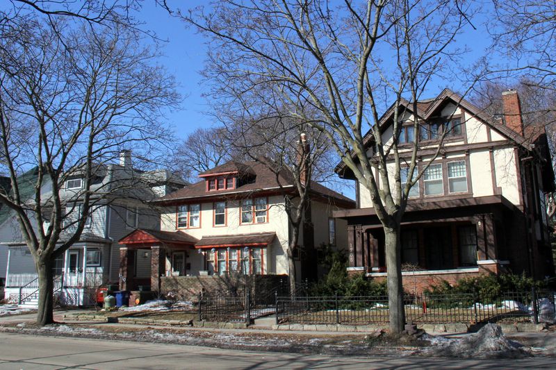 Suburban American street with three houses of various revival stylings close together and close to the sidewalk