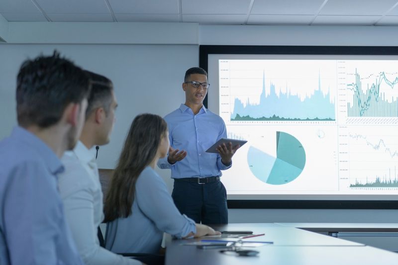 Company meeting with chart displaying metrics on big screen.