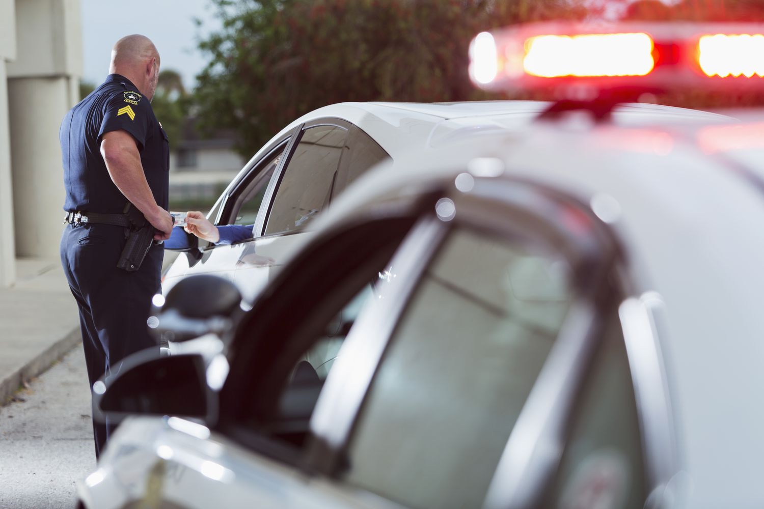 A police officer stands outside a car that has been pulled over. A hand reaches out the window and hands the police officer an ID card.