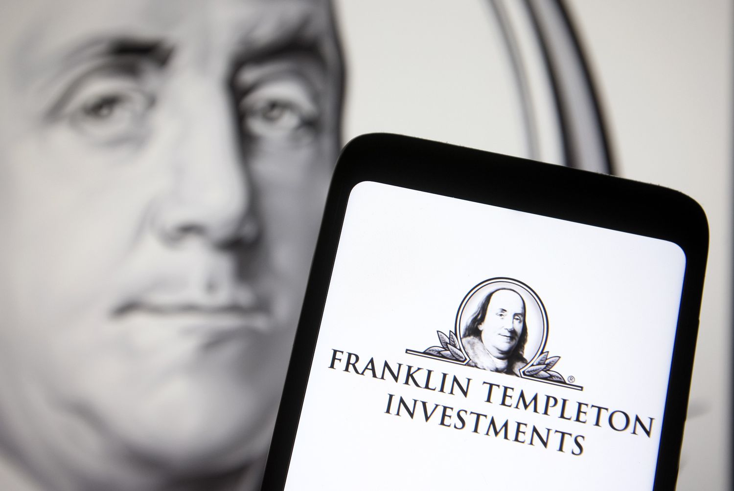 A Franklin Resources (Franklin Templeton) logo is seen on a smartphone and a PC screen in the background