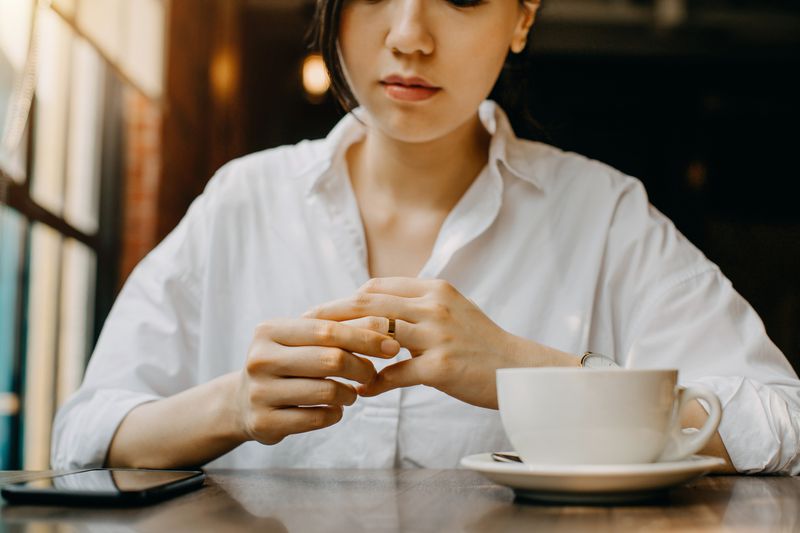 Young woman touching her wedding ring on her finger while having coffee at a cafe. 