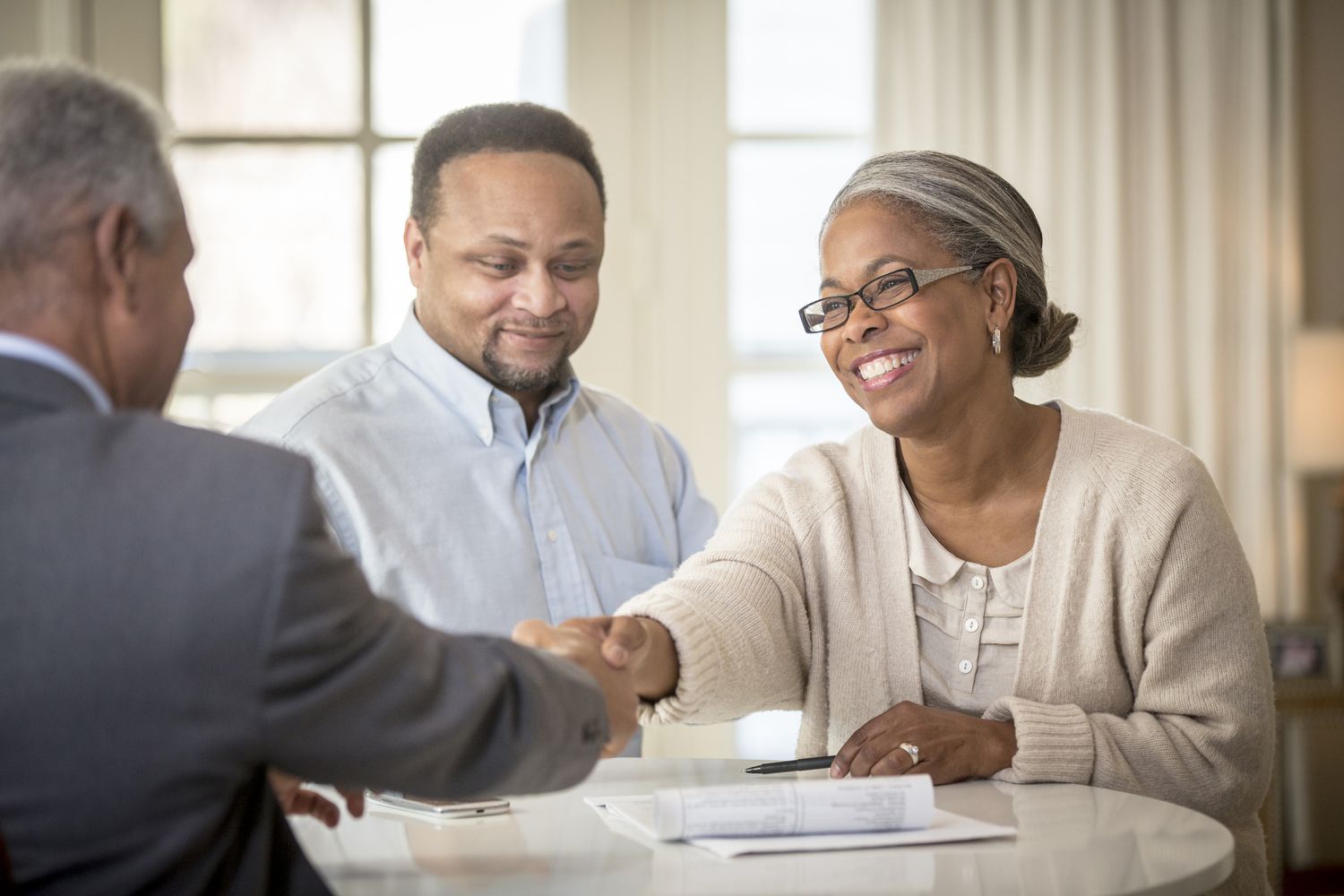 A couple sitting across a desk from their financial advisor and shaking hands