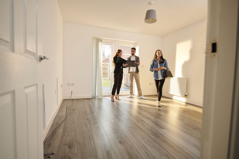 A real estate agent walks a man and a woman through a living room of an apartment