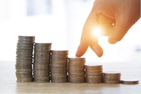 A stack of coins displayed in a decreasing way with a hand walking on it.