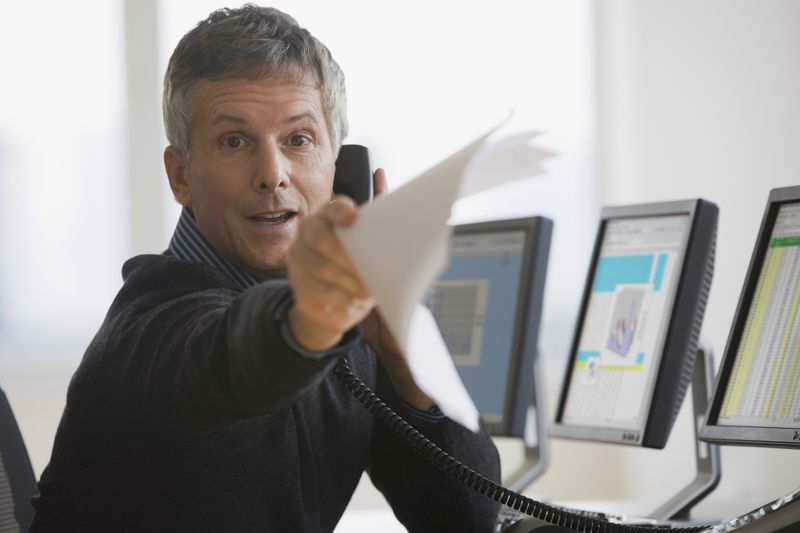 A man on the phone pointing at someone with papers