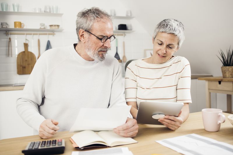 Older couple sitting in their kitchen and looking together at mortgage documents and rates on a tablet