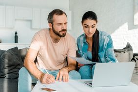 Couple in their 30s sitting on their sofa and looking at a mortgage statement and a laptop