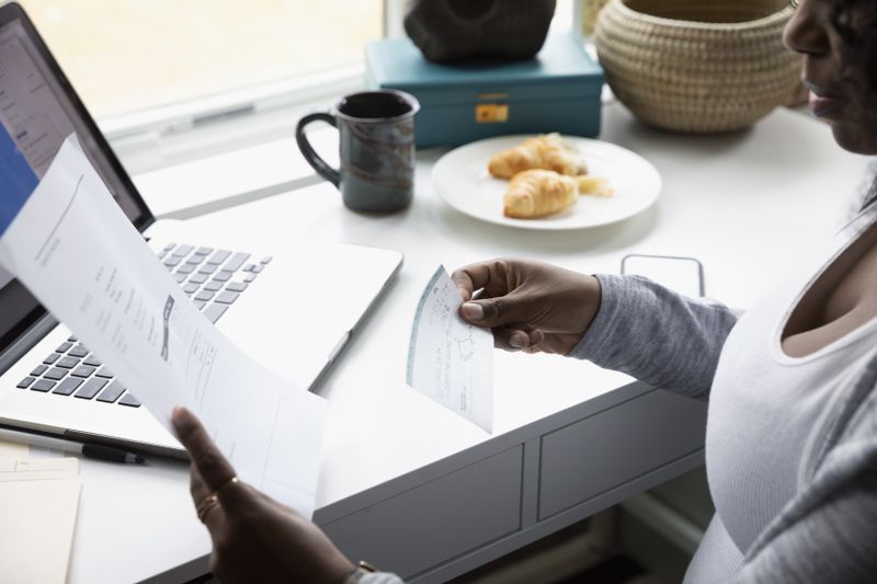 Woman with paperwork and check banking electronically on laptop