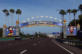Cars drive toward the entrance of Walt Disney World in Florida, through an arch with Mickey and Minnie Mouse on each side.