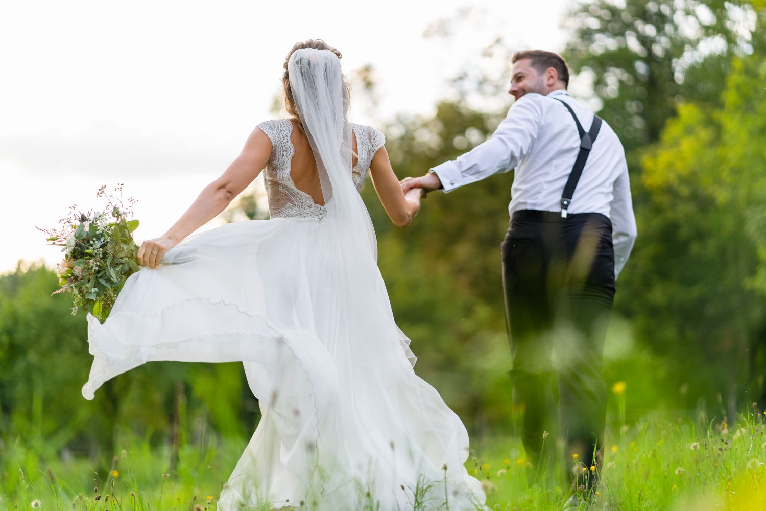A man and a woman who just got married hold hands and walk in an open field.