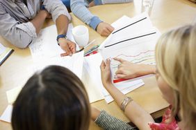 A person points at a line chart at a table with three other people who are reviewing documents