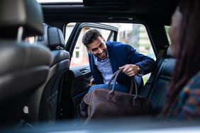 Businessman entering a car, holding luggage, his friends sitting in car and waiting for him