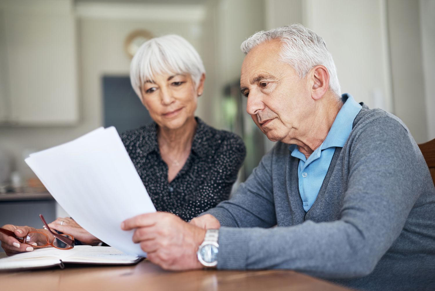 An older adult couple sit at a table to review a monthly pension statement showing the net assets available for benefits.