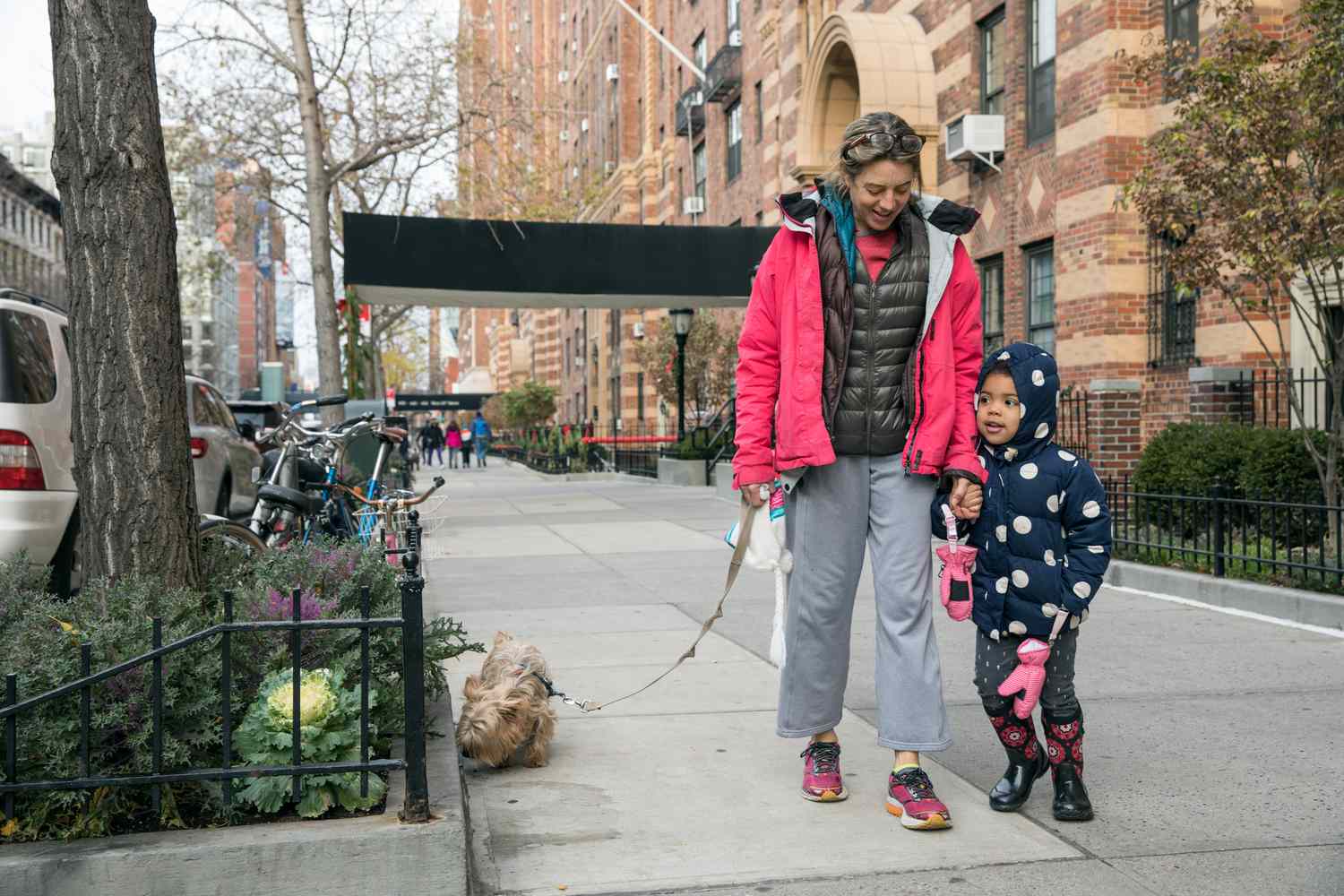 A woman walks with her child and a dog on a leash in New York City