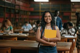 A student holding a yellow book in a college library
