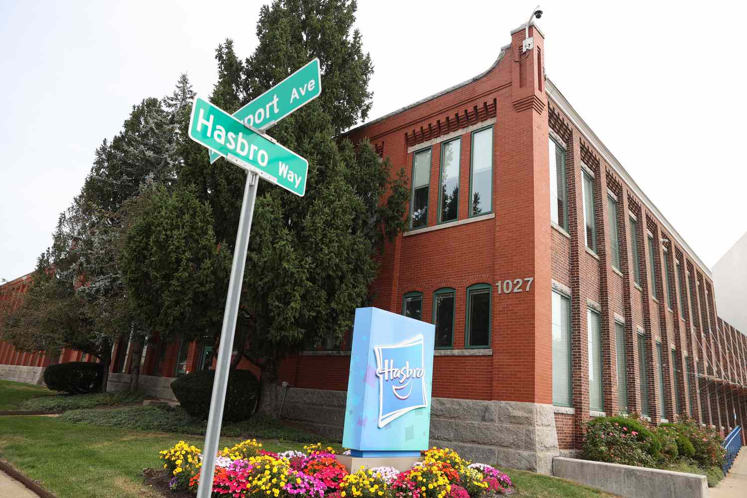 The Hasbro headquarters is seen with a blue Hasbro sign and a green Hasbro Way street sign in front of the building.