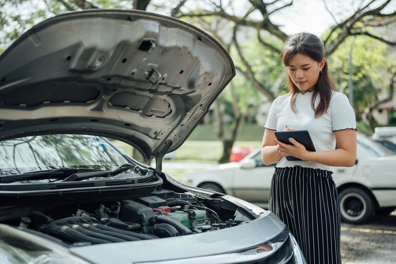 Automobile insurance adjuster uses digital tablet to inspect damage to vehicle.