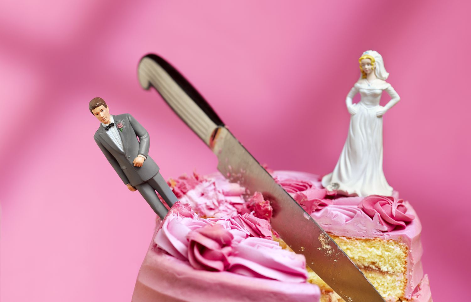 A cake with a bride and groom figurine, a knife cutting into the middle