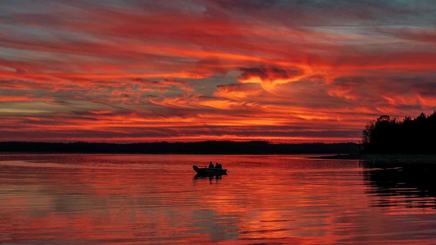 A small boat with two people on Percy Priest Lake at sunset. 