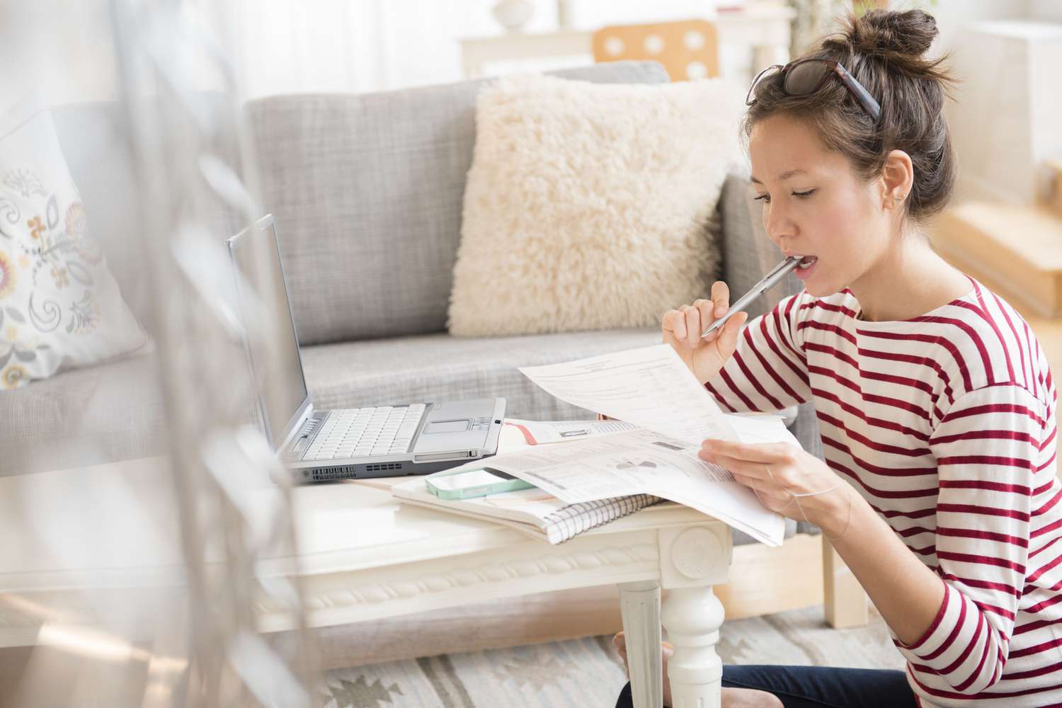 Woman looking at paperwork with a laptop at home