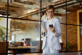 Woman wearing striped pantsuit in modern office looking down at her cellphone.