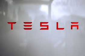 The red Tesla logo is seen on a white charging station.