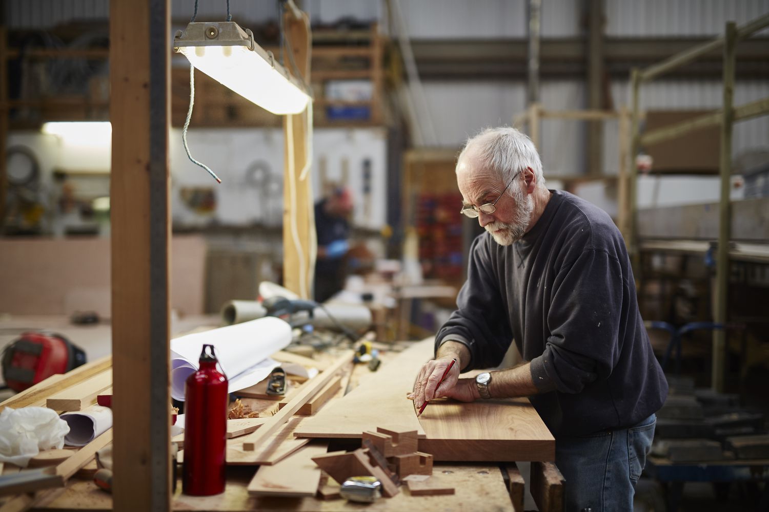 A man measures wood in an industrial workshop. 