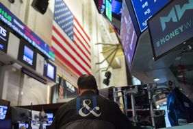 A trader works at a desk on the floor of the New York Stock Exchange, sitting with his back to the camera beneath an American flag.