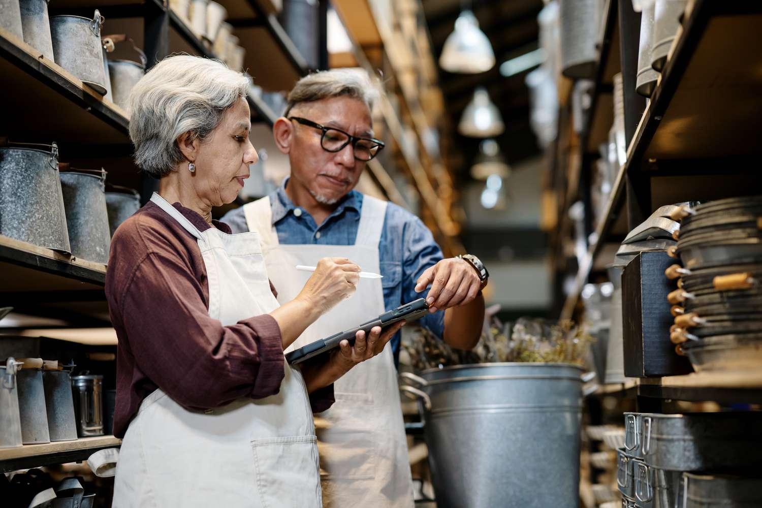 Two older adults with a table and stylus standing in an aisle with equipment and products all around them. 