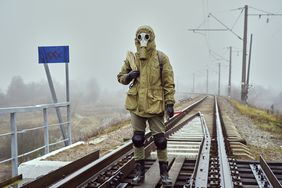 A doomsday prepper with a gas mask and rope over the shoulder on train tracks.