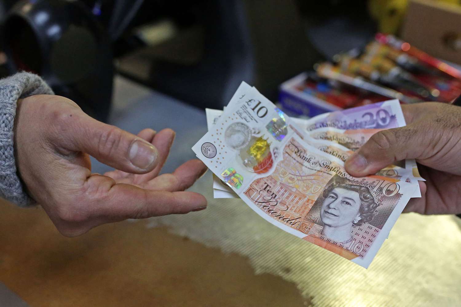 A close-up of two hands exchanging British pound notes as a shopkeeper passes a customer change.